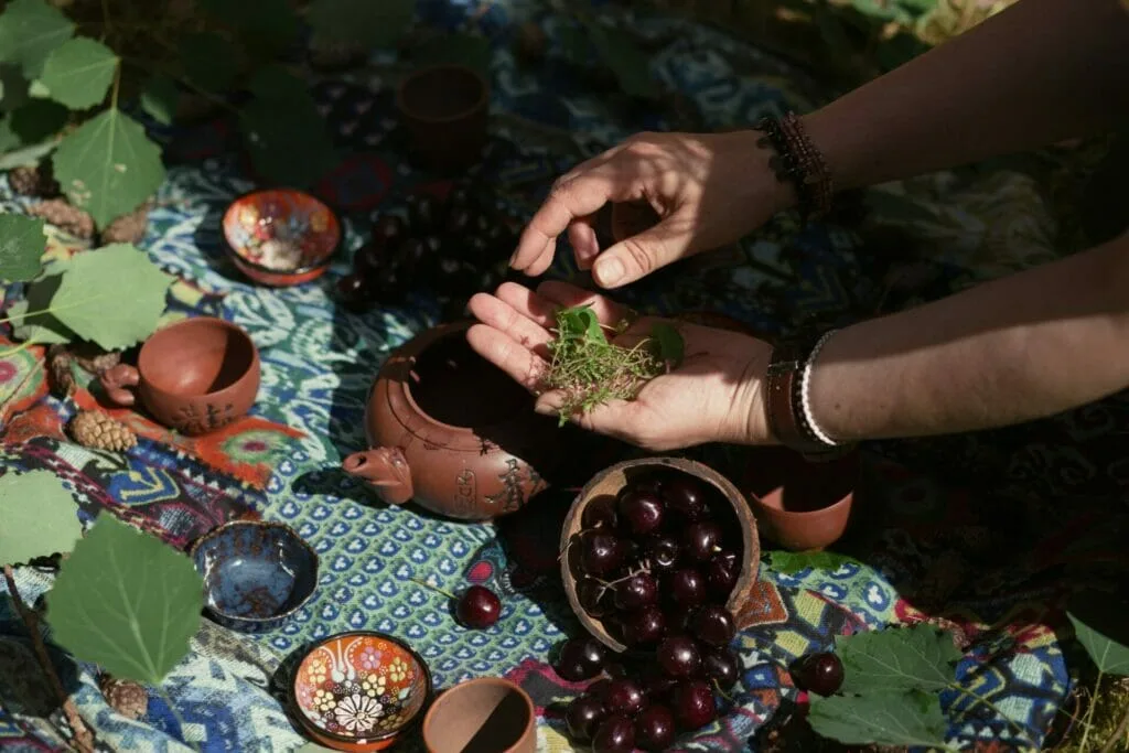 Miško maudynės: rankos laiko žoleles prie arbatos rinkinio su vyšniomis