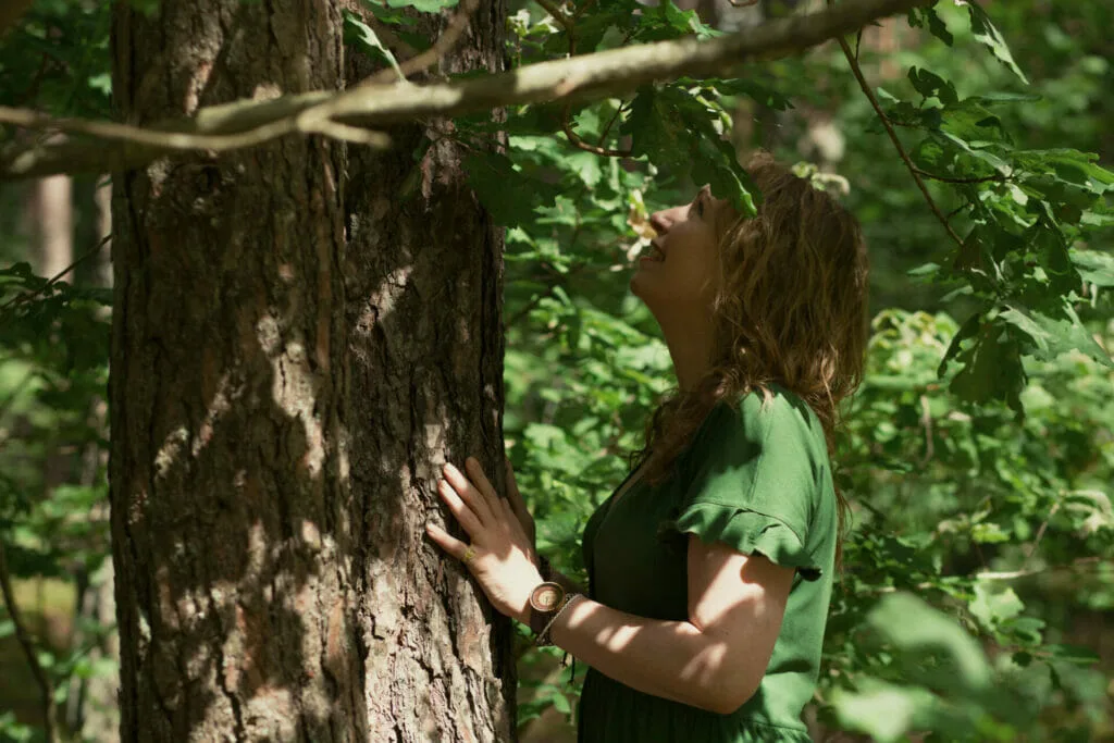 Moteris prisiglaudusi prie medžio miške, miško maudynės