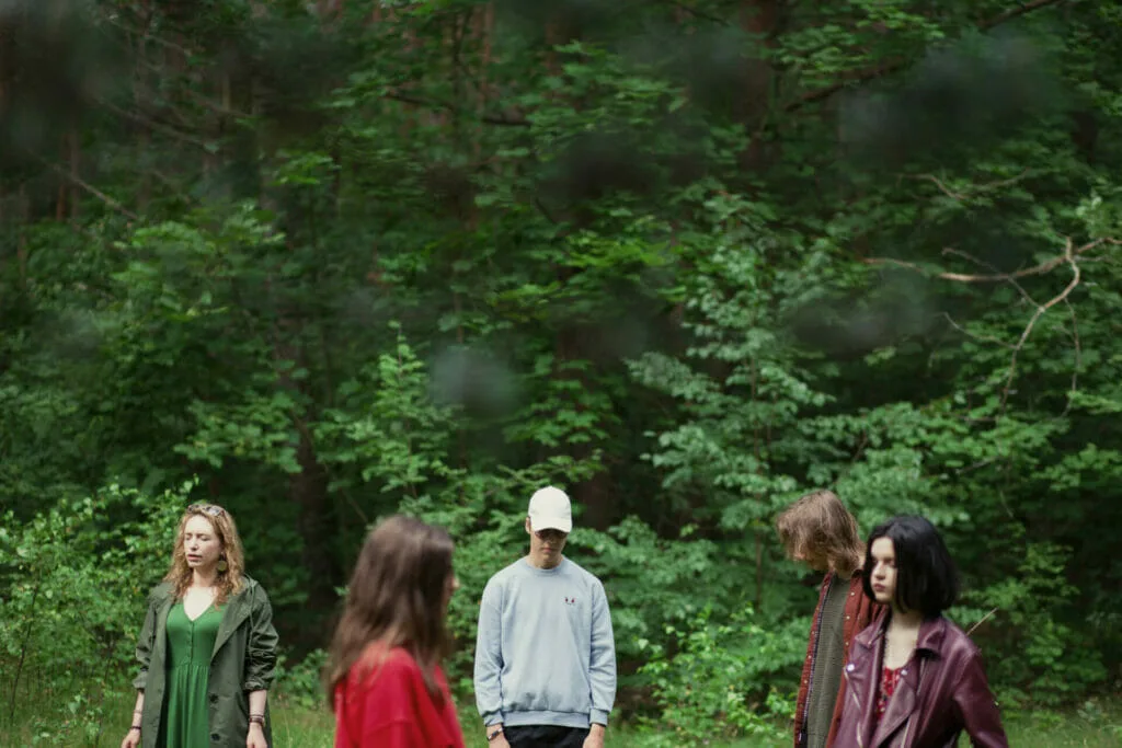 Grupė žmonių miške, galbūt dalyvauja "Miško maudynėse". Žalia gamta, jauni žmonės.